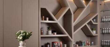 A modern bathroom with a beige vanity, a white vase with flowers, and shelves with toiletries.
