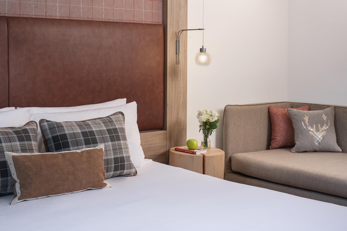 Een hotelkamer met een bed, een bank, een nachtkastje met een lamp en een tafeltje met een vaas en een appel.