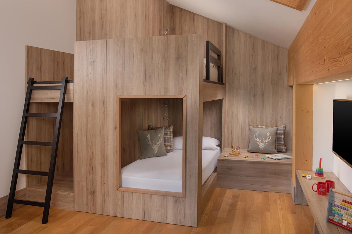Een kleine kamer met een stapelbed, een trapje, een bureau met speelgoed en een televisie.