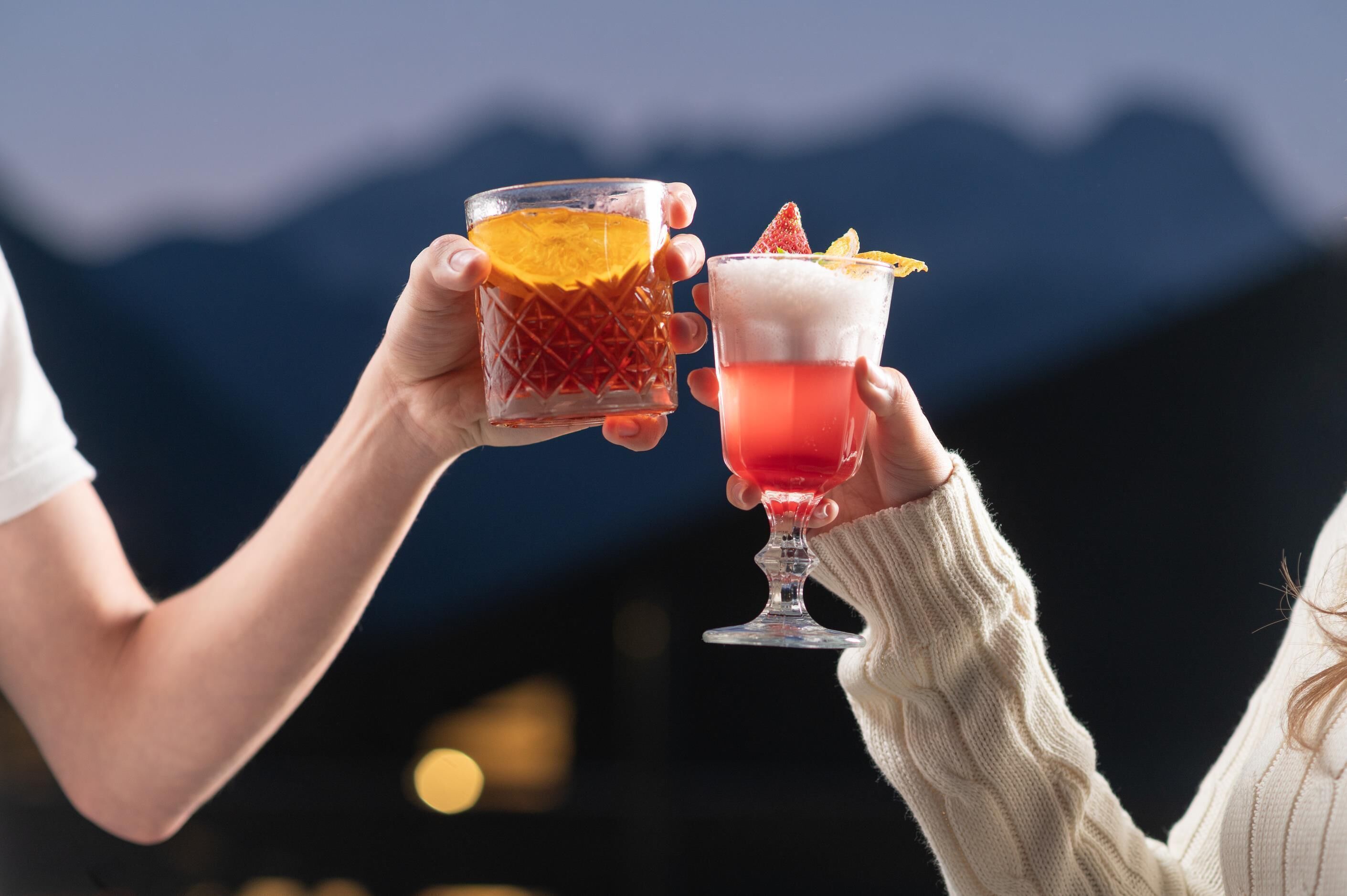 Due persone che sorseggiano cocktail con montagne sullo sfondo.