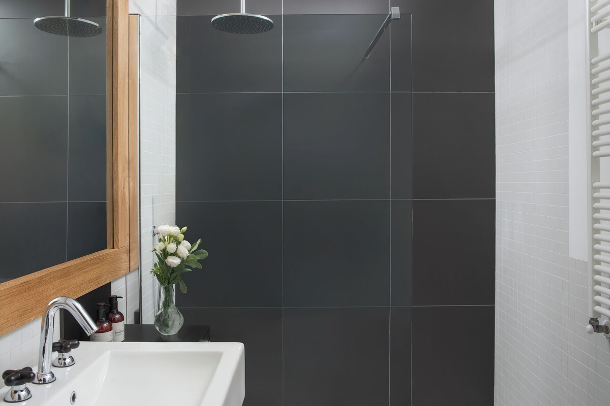 A modern bathroom with a white sink, two showerheads, and a wooden-framed mirror.