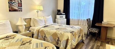 Habitación de hotel con dos camas, un escritorio, una silla, una ventana con cortinas, una lámpara y una obra de arte colgada en la pared.