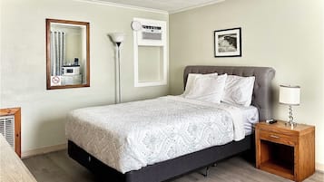 A neatly arranged hotel room with a bed, a bedside table with a lamp, a mirror, and a framed picture on the wall.
