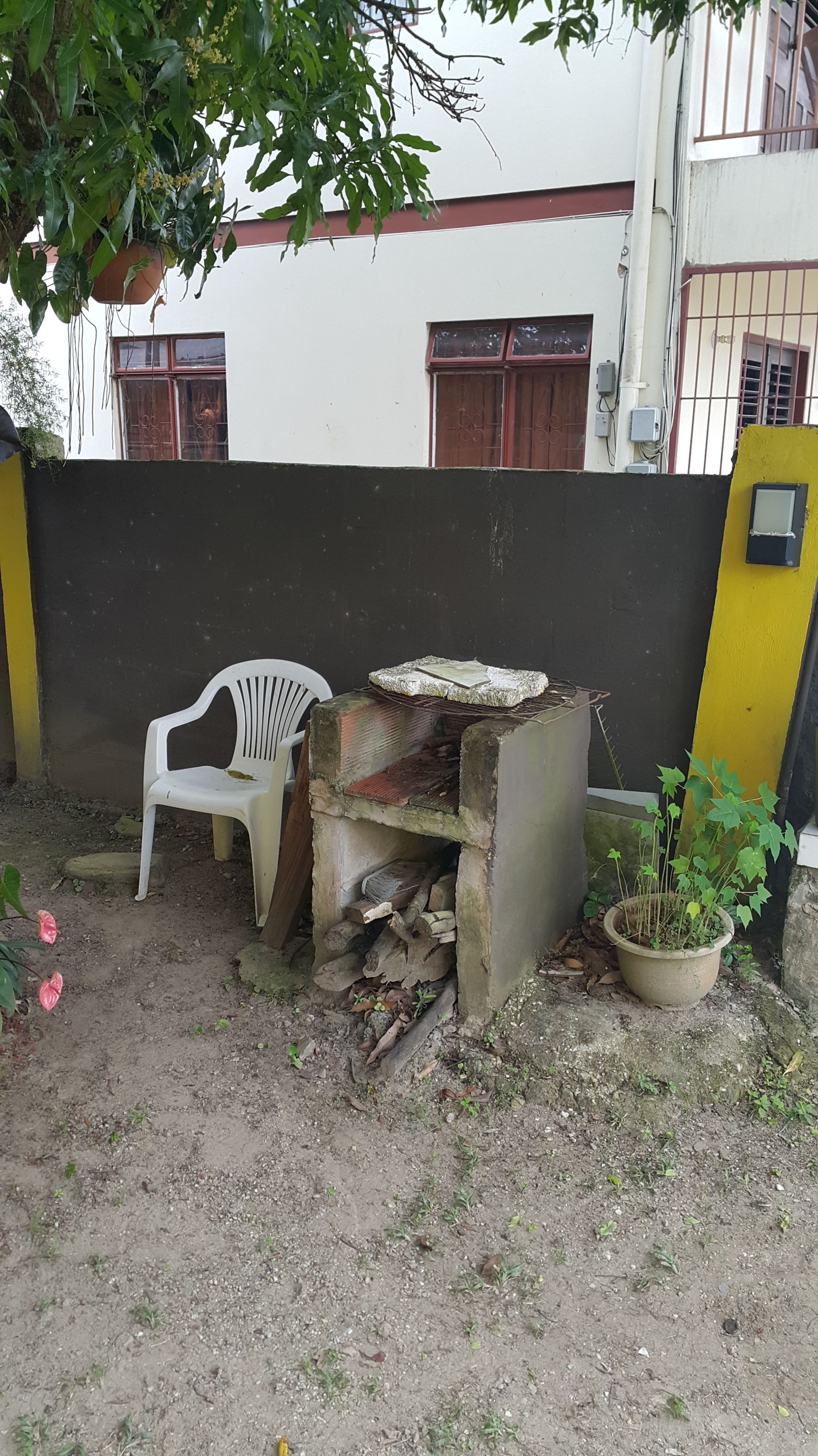 A makeshift outdoor cooking area with a brick oven, a plastic chair, and a potted plant.