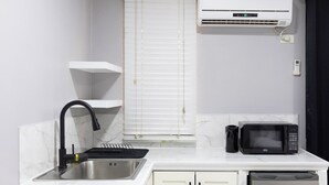 A kitchen with a sink, a microwave, a refrigerator, and a window with blinds. - Tony's Guest House (Diego Martin)