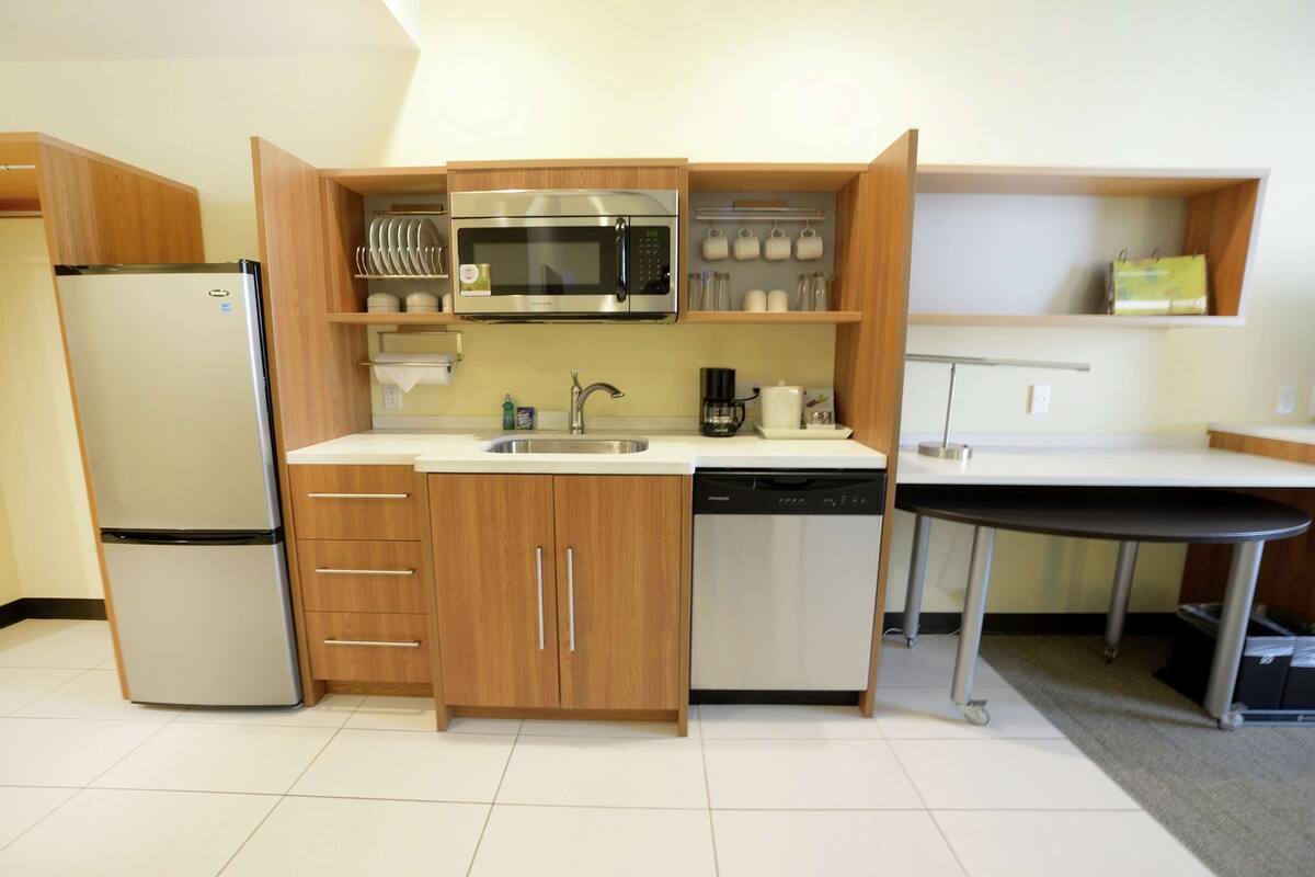 A compact kitchen with a built-in microwave, stainless steel refrigerator, and dishwasher.
