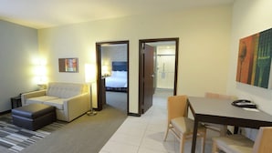 Ein Hotelzimmer mit einer Couch, einem Esstisch mit Stühlen, einer Lampe und einem Bett im Hintergrund.