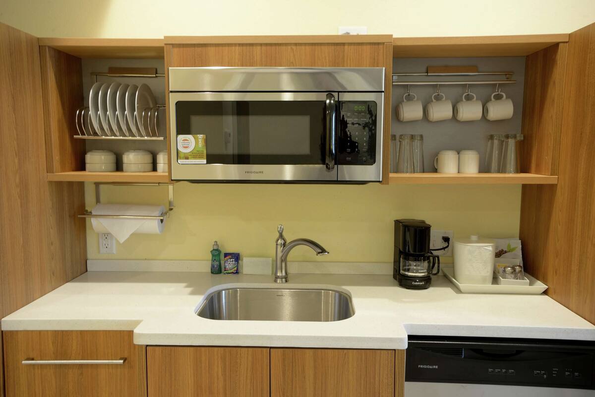 A compact kitchen with a stainless steel microwave, a sink, and a coffee maker.