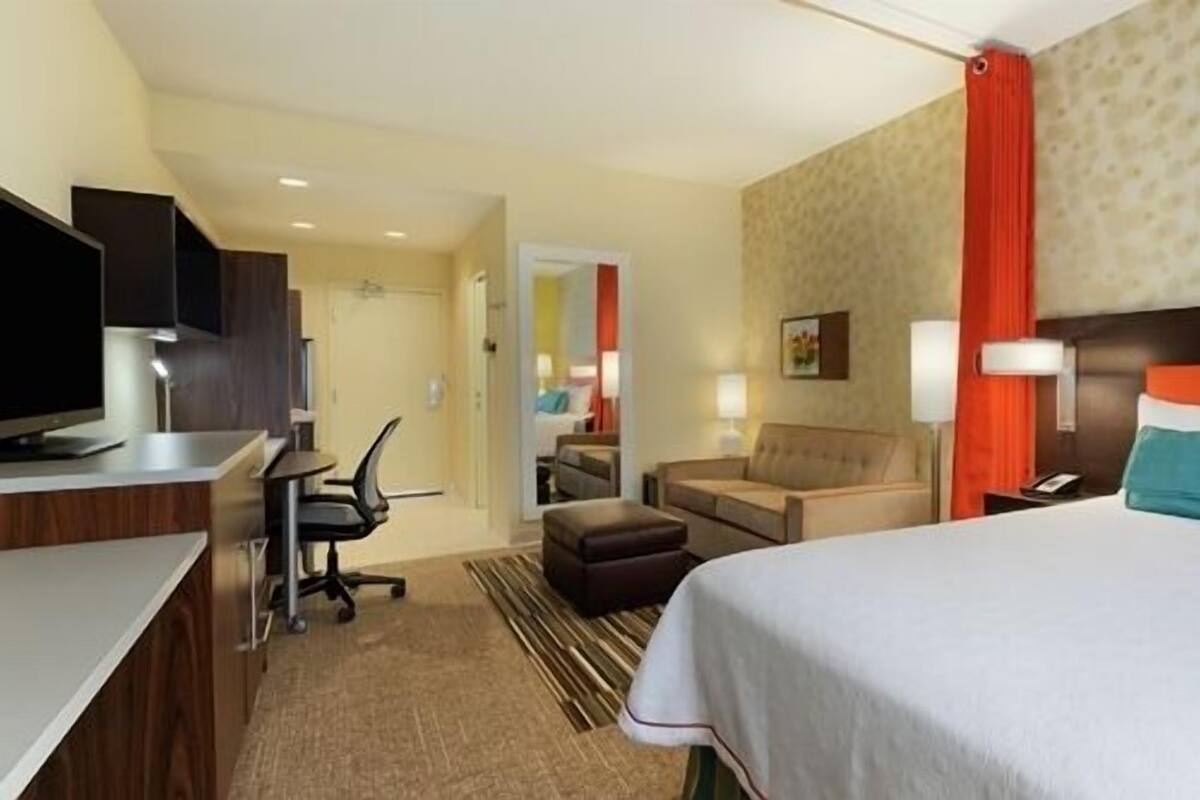A hotel room with a bed, a desk, a chair, a sofa, and a television.