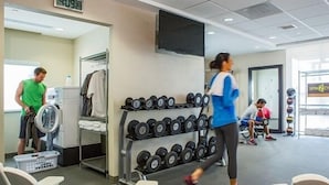 Ein Fitnessstudio mit Laufband, Kurzhanteln und einem Fernseher an der Wand.