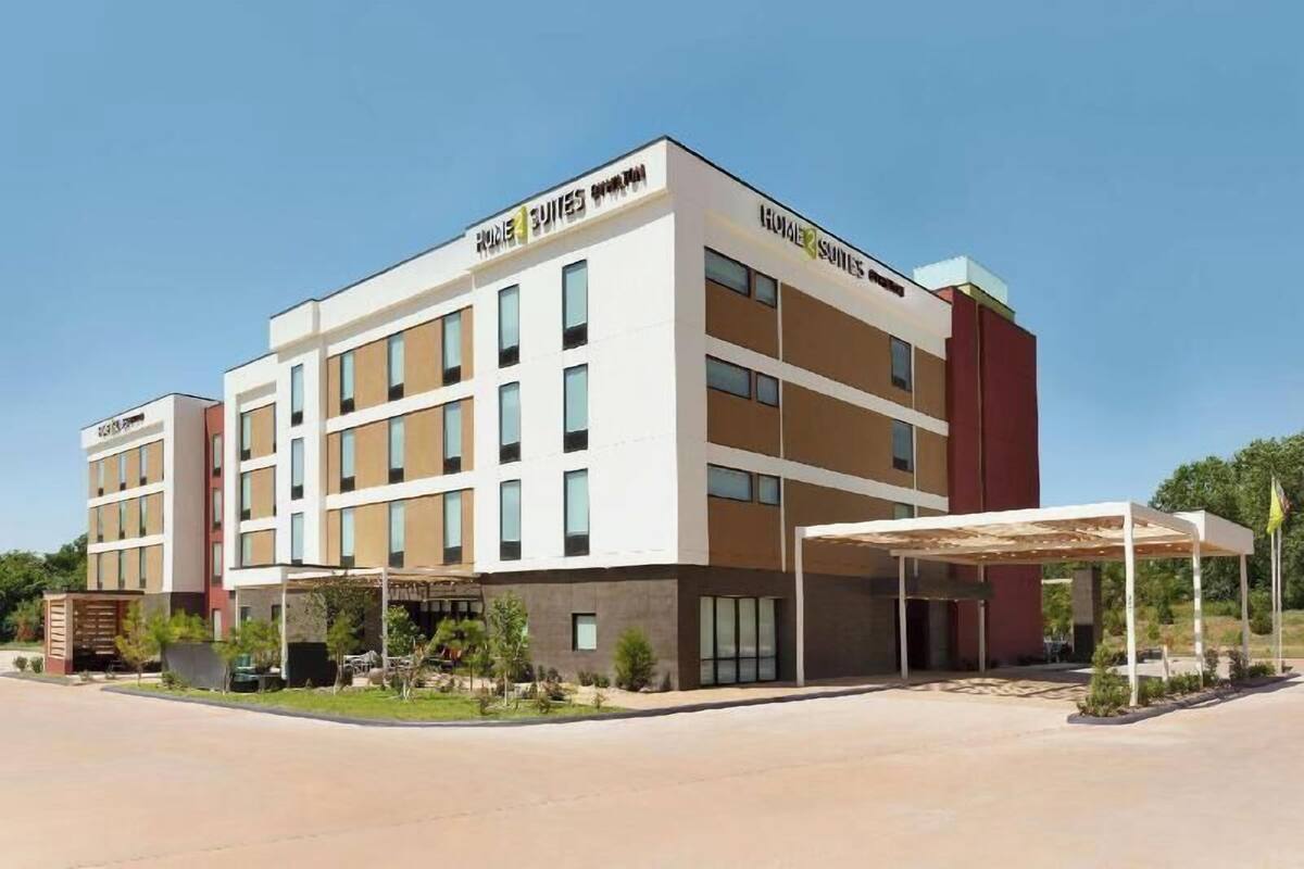 A modern hotel with multiple floors, a covered entrance, and a landscaped area with small trees.