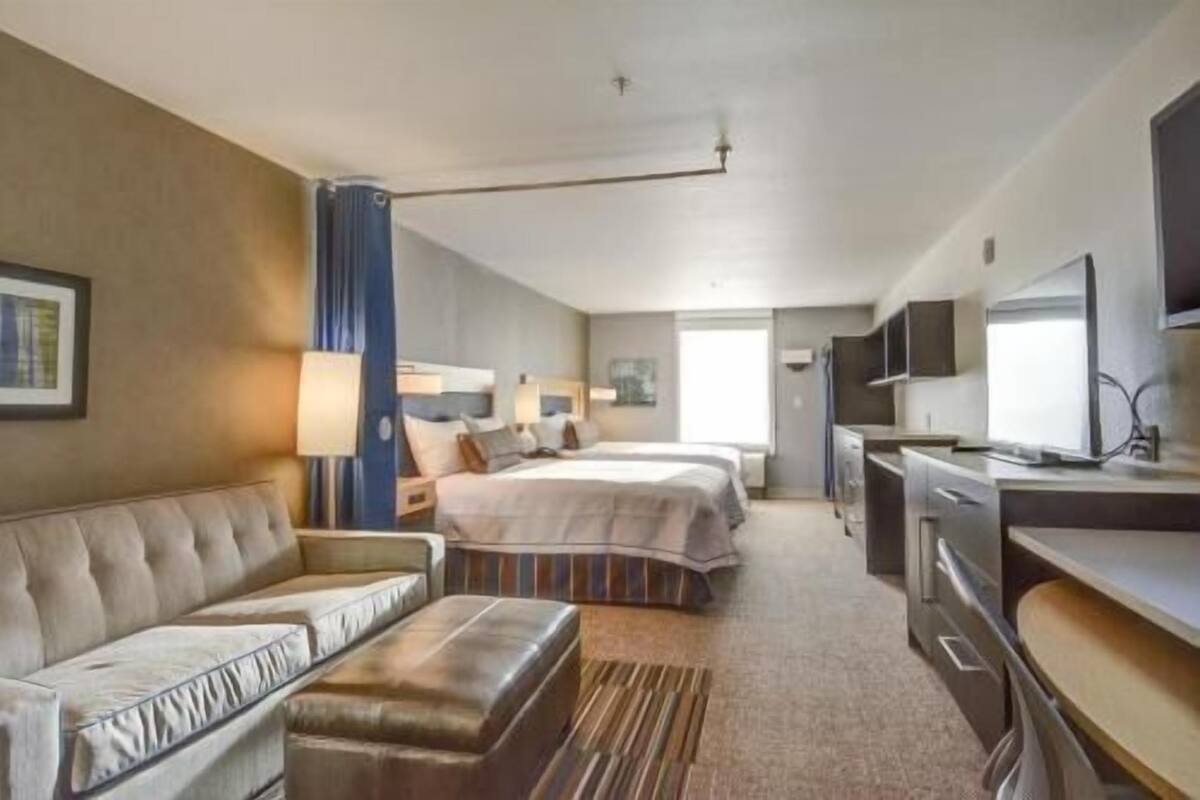 Une chambre d’hôtel avec un canapé, deux lits, une télévision et une kitchenette.
