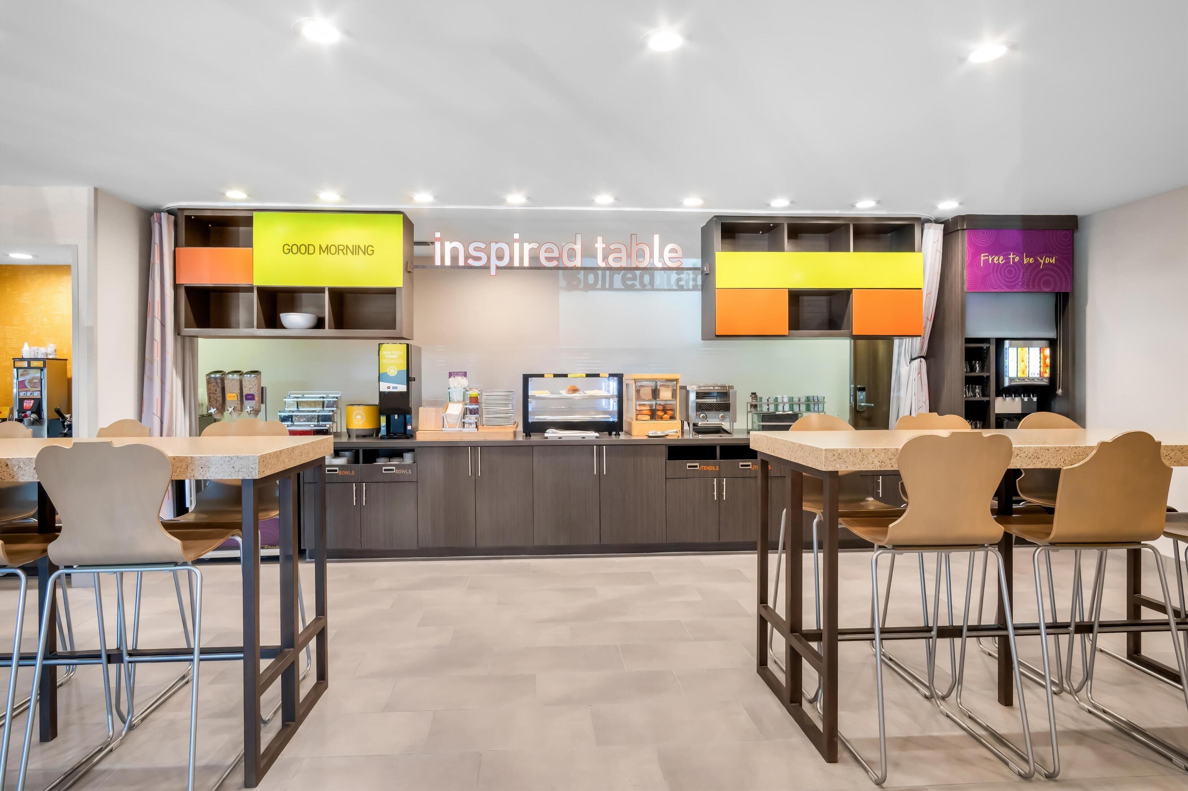 A modern dining area with a long table, chairs, and a counter with a coffee machine.