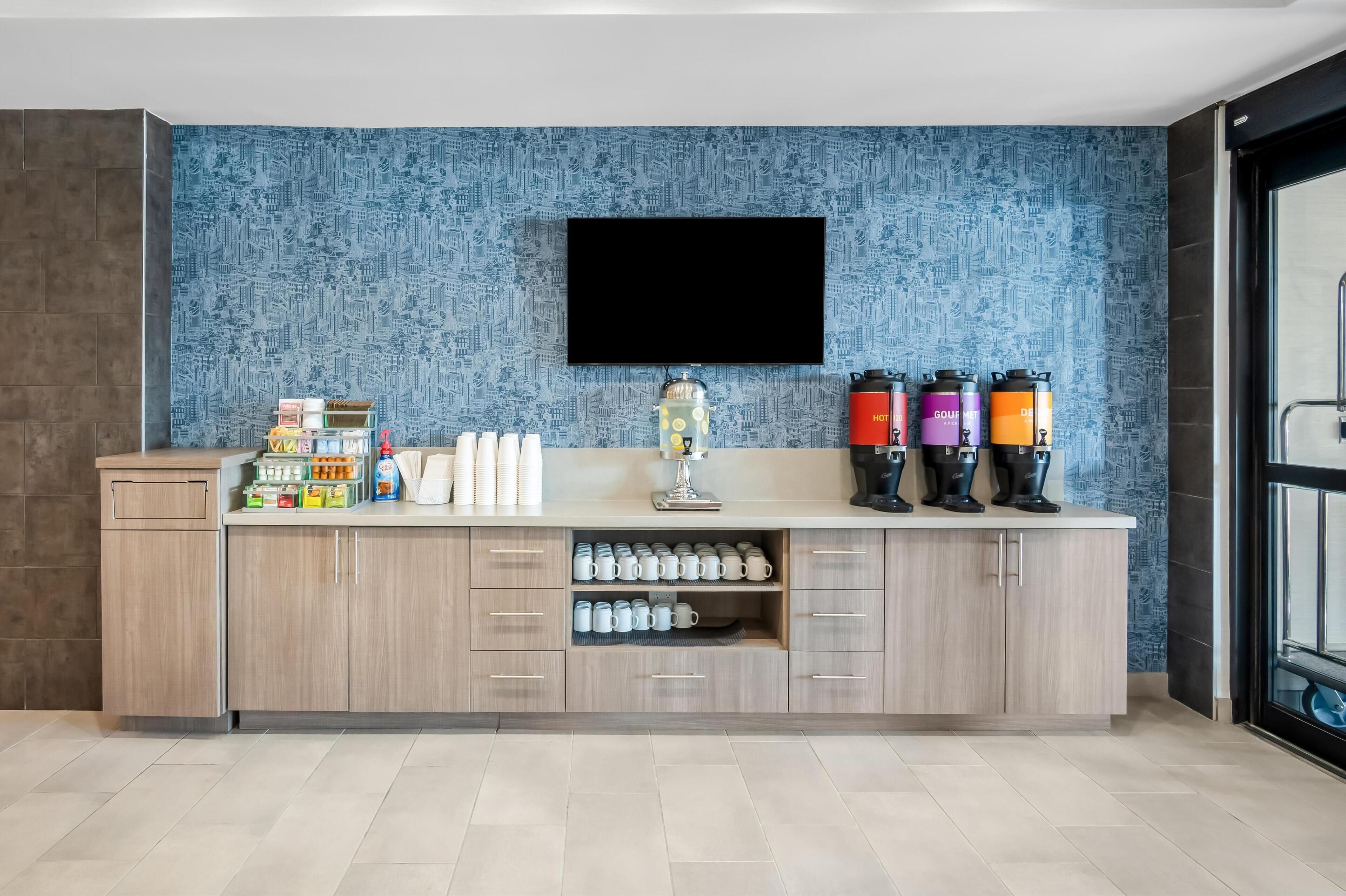 A modern kitchen with a flat-screen TV, coffee makers, and storage cabinets.