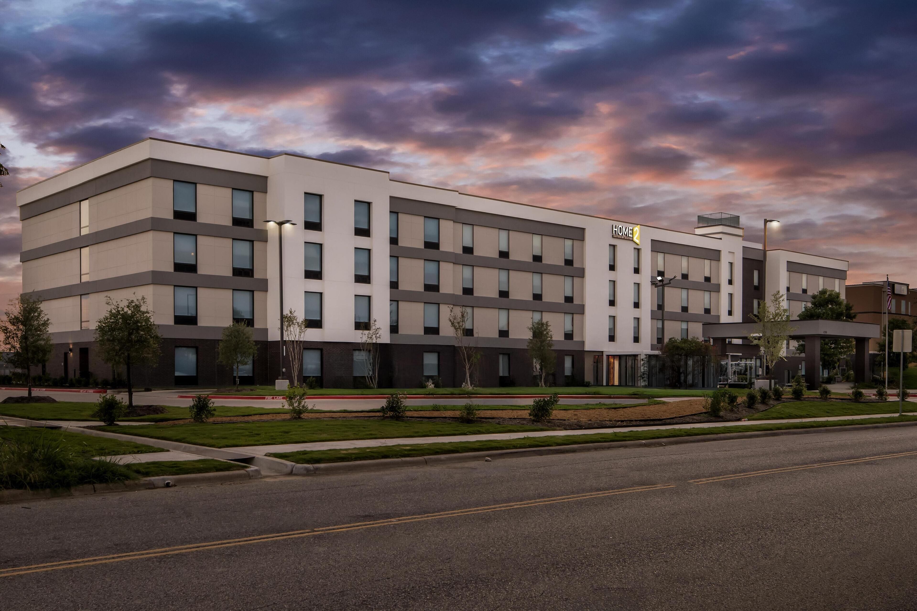 A modern hotel with a flat facade, multiple windows, and a well-maintained lawn.