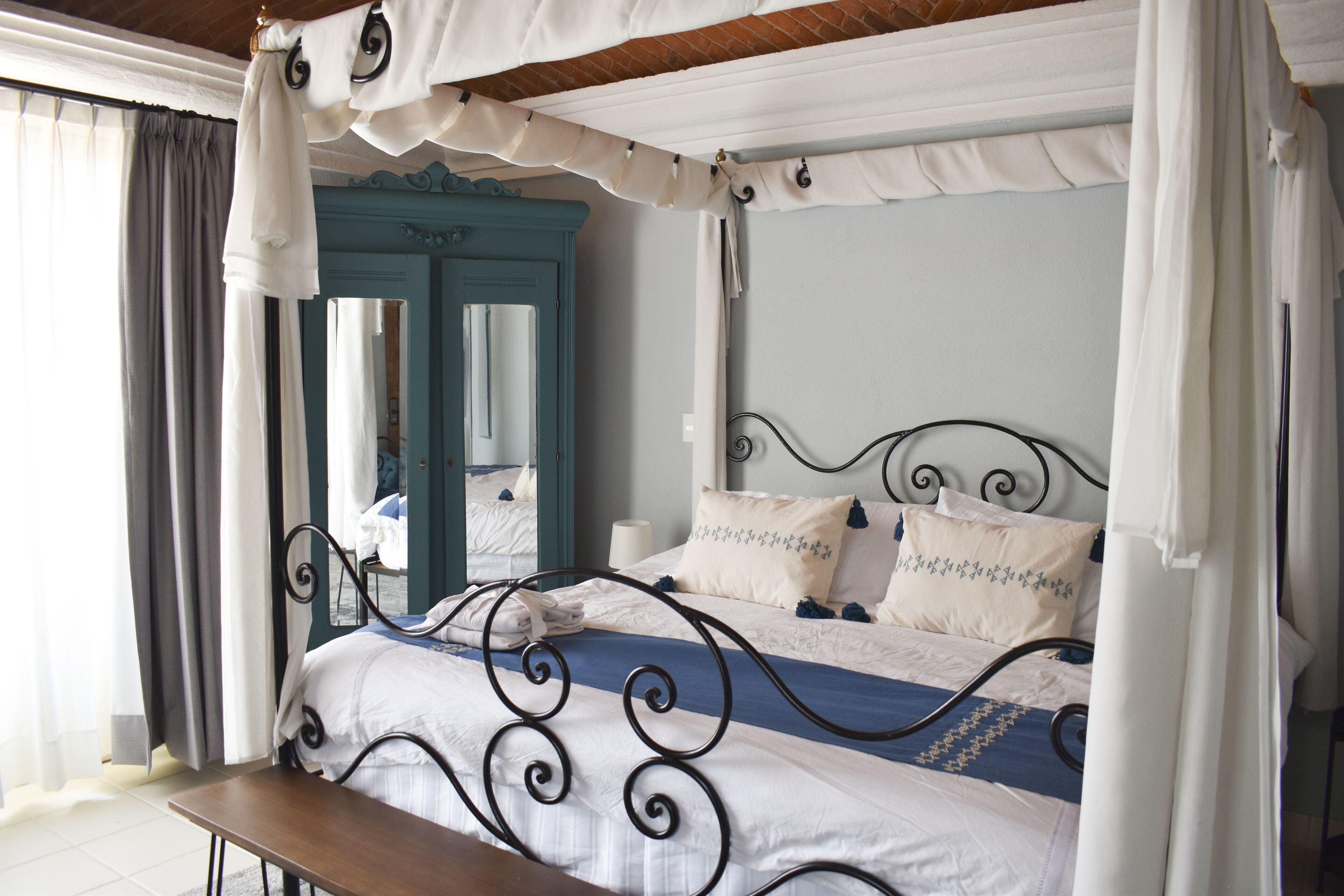 A bed with a canopy, a bench, a mirror, and a door with a blue frame.
