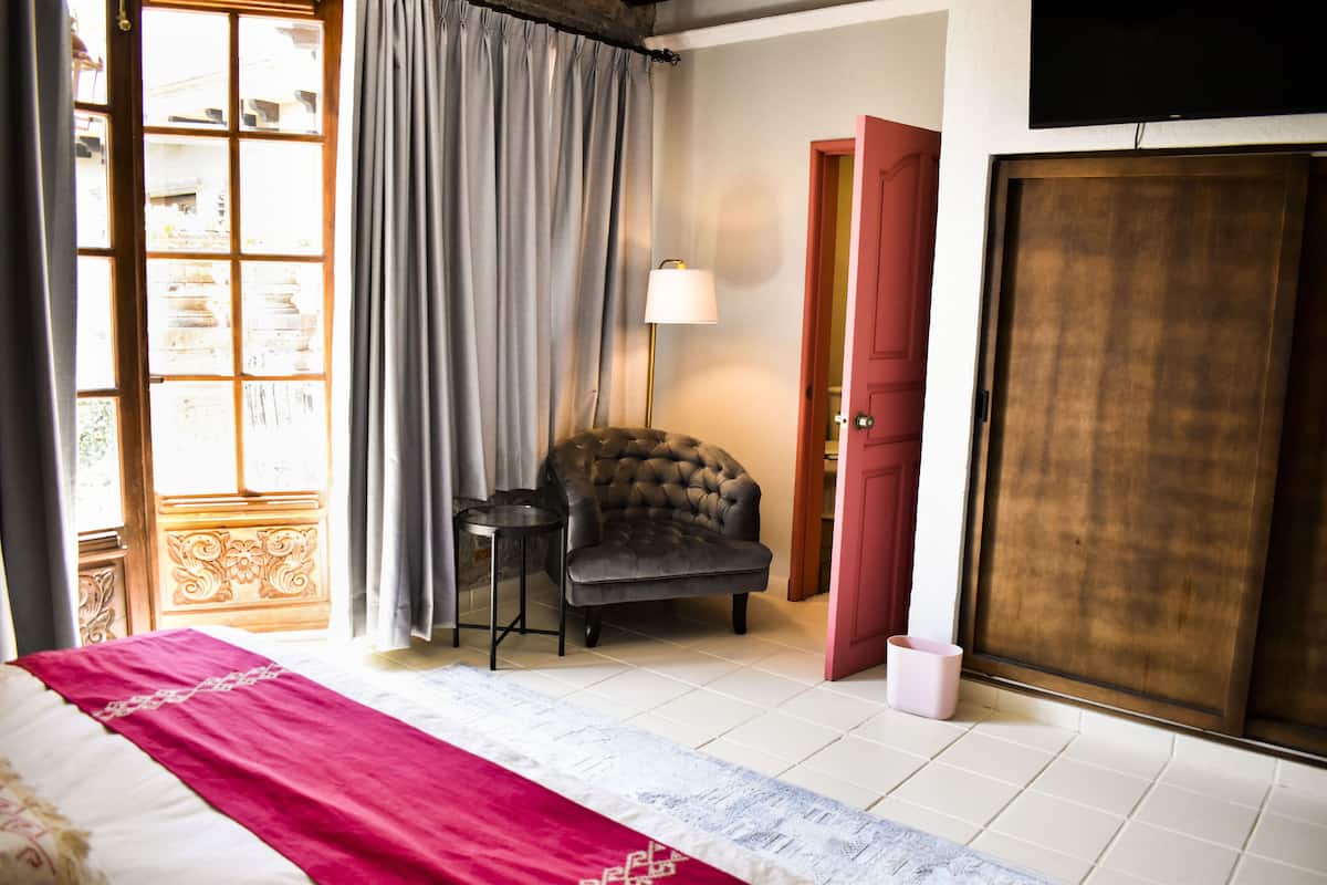 A bedroom with a bed, a chair, a lamp, a wardrobe, and a window with curtains.