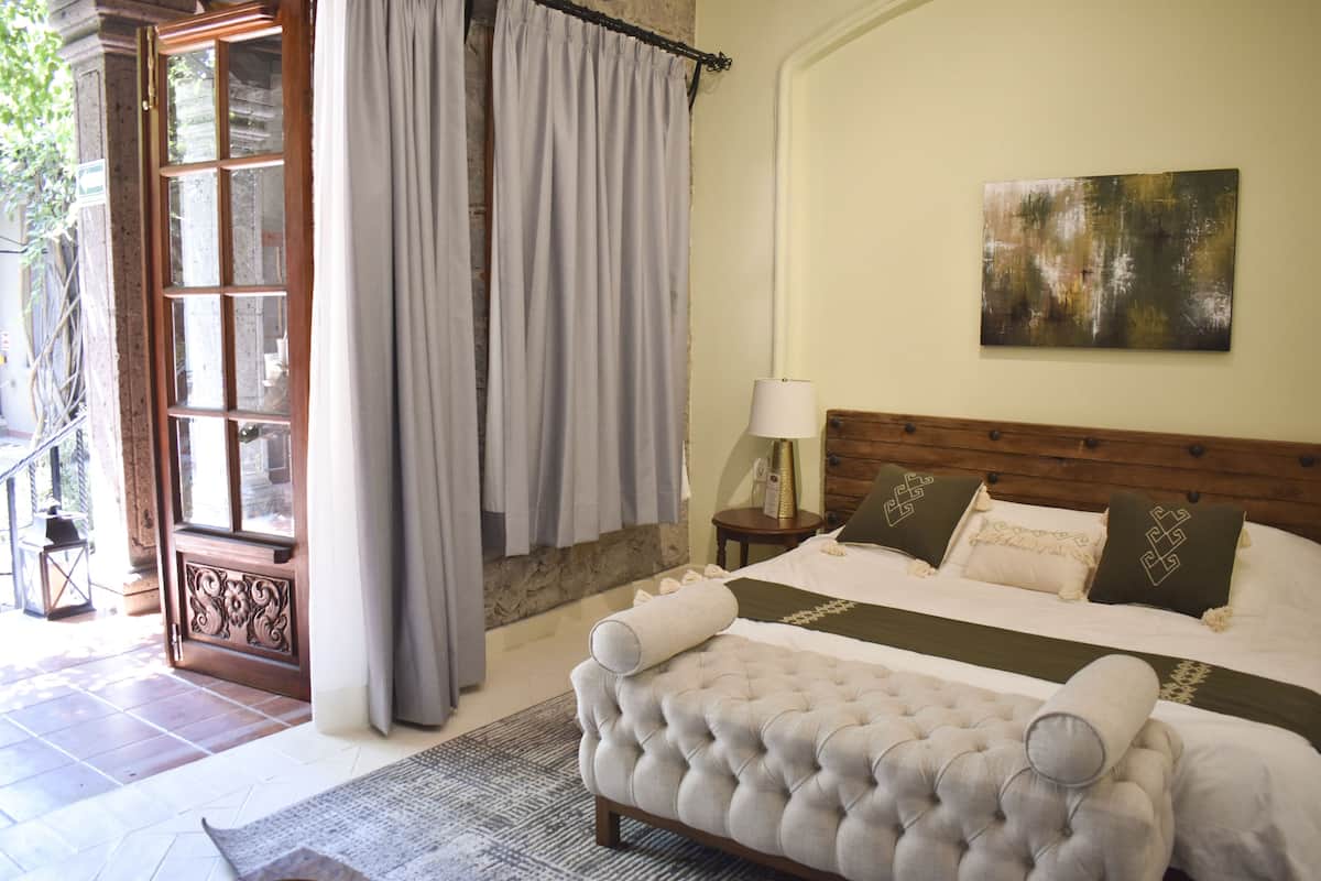 A bedroom with a large bed, a wooden headboard, a nightstand with a lamp, and a painting on the wall.