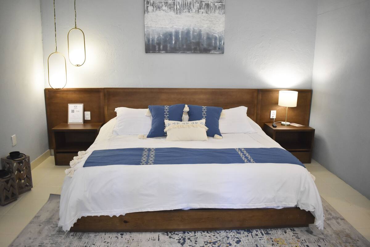 A neatly made bed with a blue and white bedspread, two bedside tables with lamps, a framed certificate on the left table, and a wooden headboard.