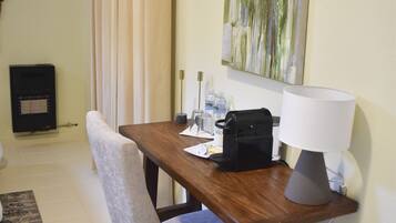A hotel room with a wooden desk, a chair, a lamp, a painting on the wall, and a radiator.