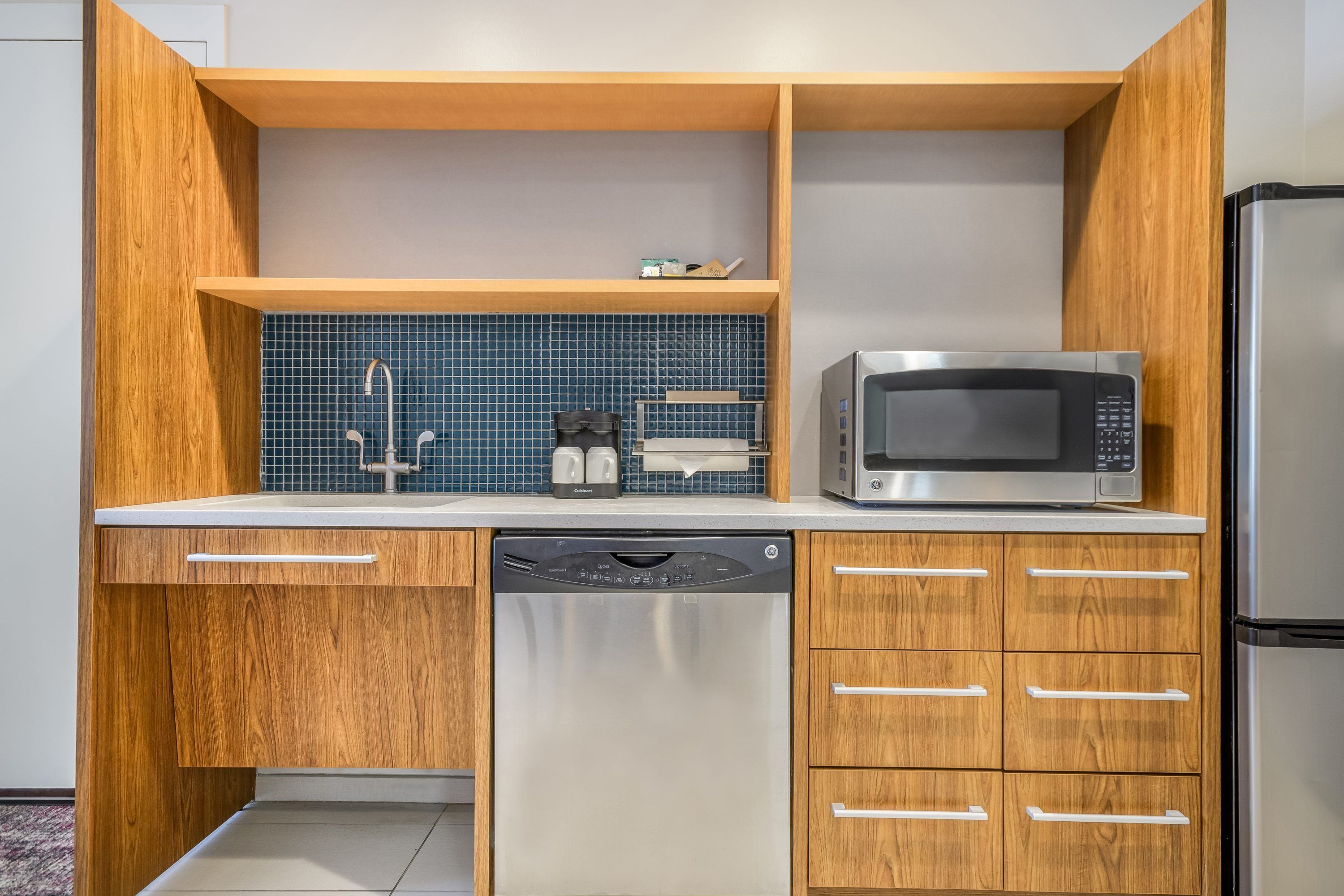 A compact kitchen with wooden cabinetry, a dishwasher, a microwave, and a refrigerator.