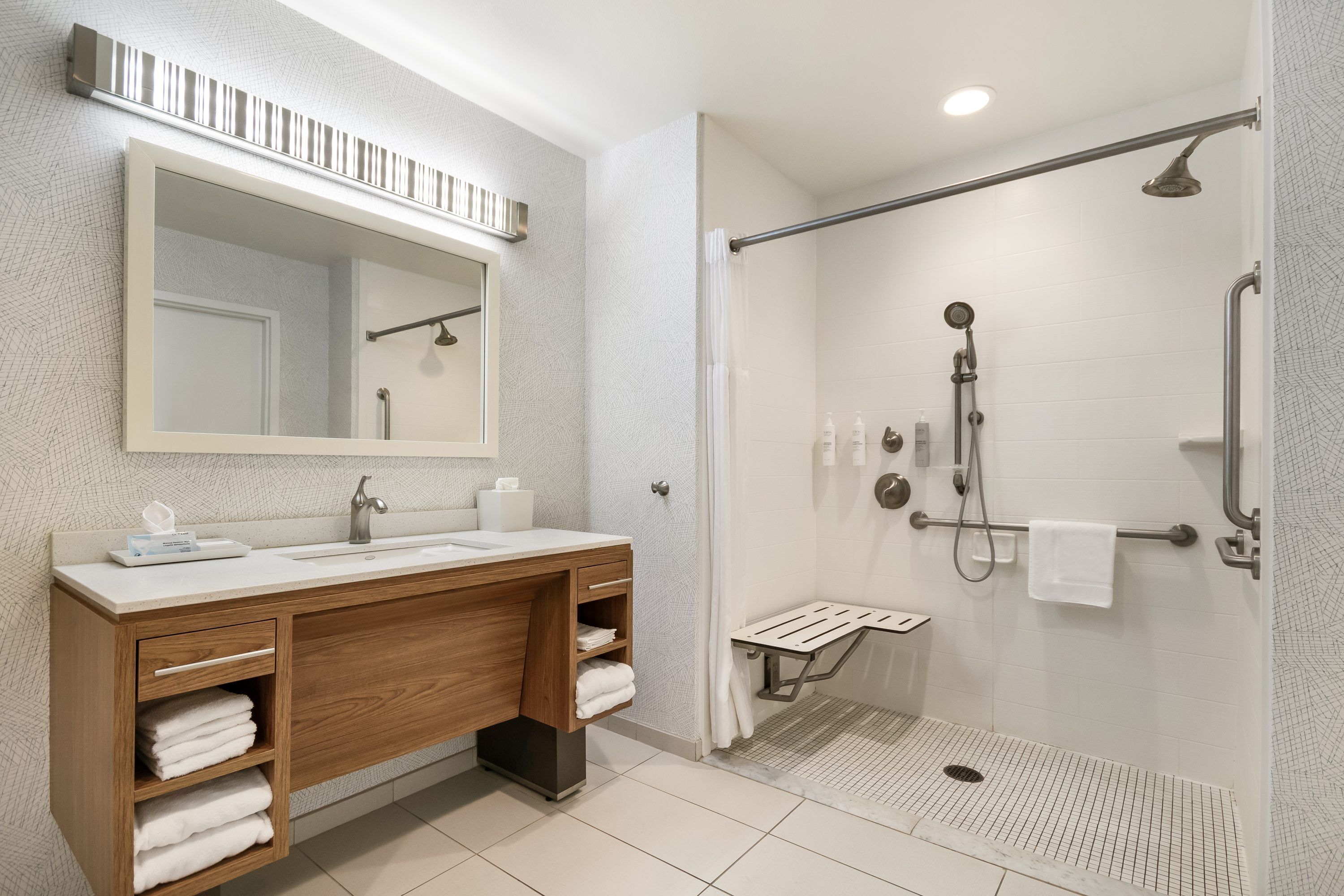 A modern bathroom with a wooden vanity, a large mirror, a shower with a handheld showerhead, and a towel rack.