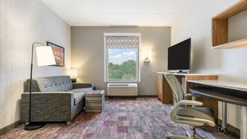A hotel room with a sofa, a desk, a chair, a television, a window with a view, and a patterned carpet.
