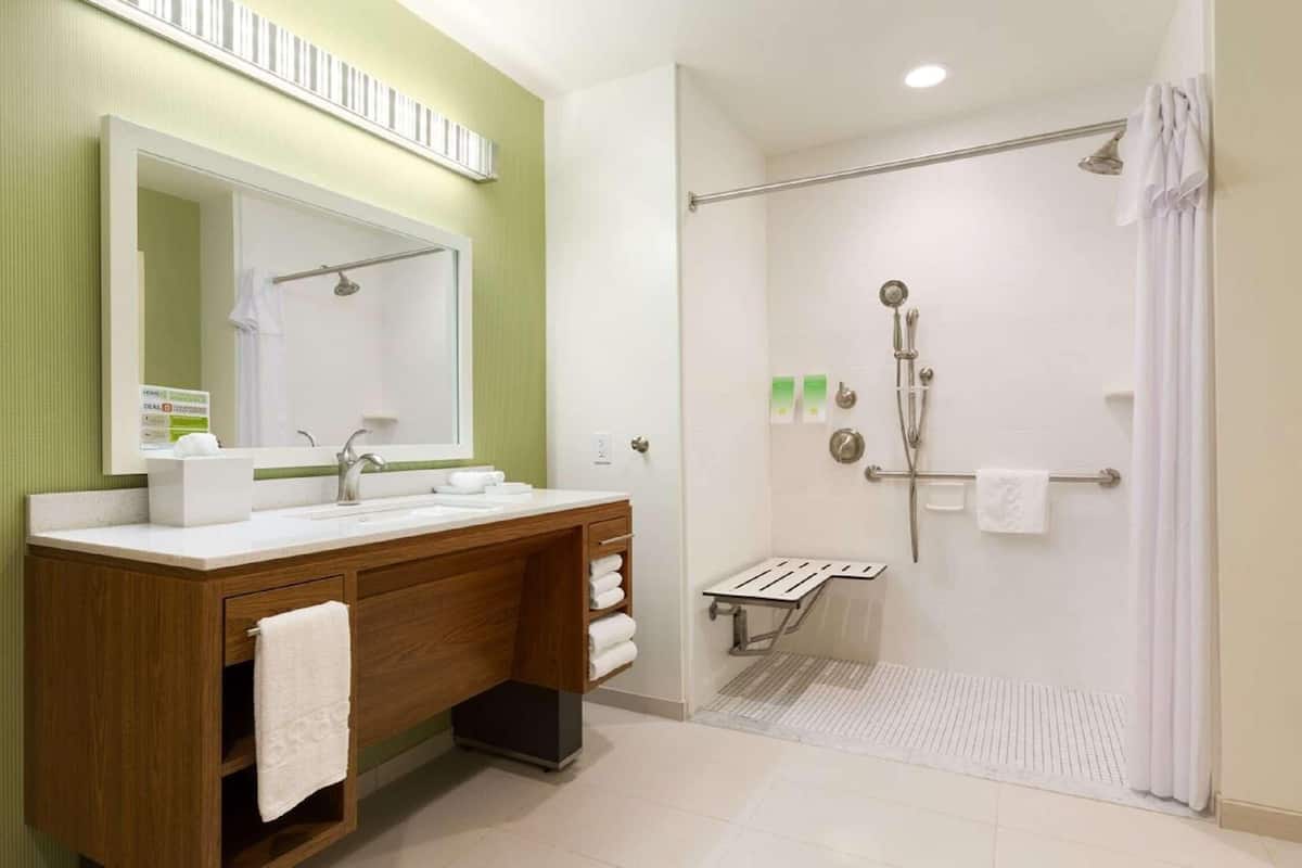 A bathroom with a wooden vanity, a large mirror, a shower with a glass door, and a towel rack.