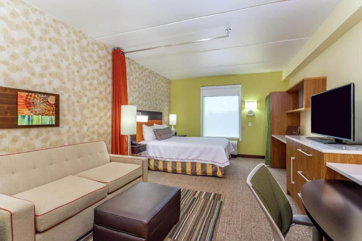 A hotel room with a sofa, a bed, a desk, a television, and a window.