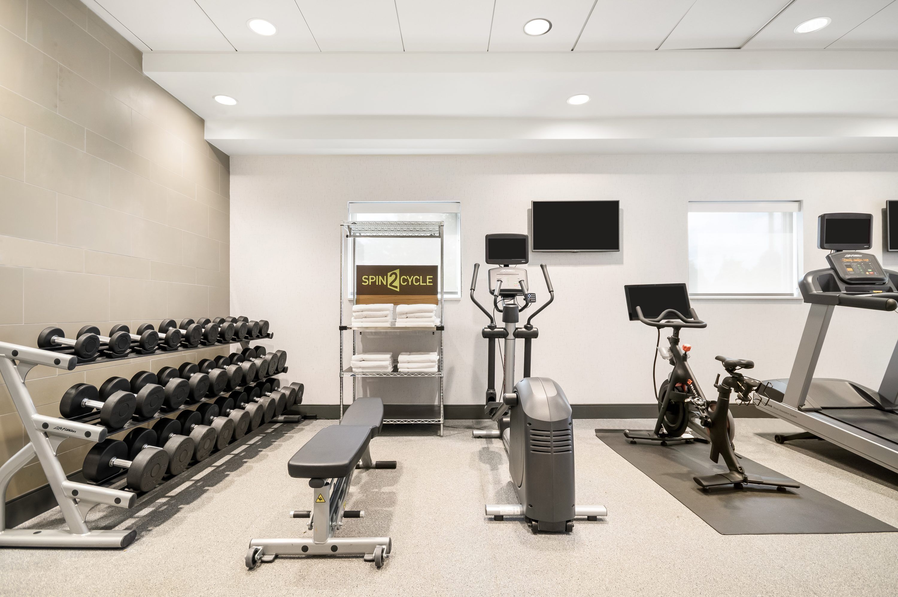 A gym with dumbbells, a bench, cardio machines, and a treadmill.