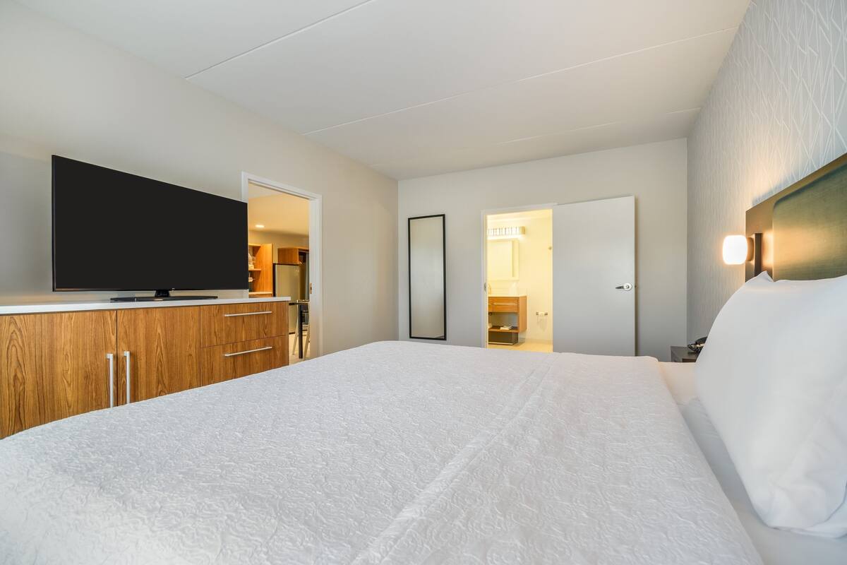 A hotel room with a large bed, a flat-screen TV, wooden cabinets, and a mirror.