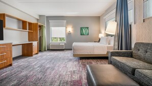 A hotel room with a bed, a sofa, a desk, and a wardrobe. - Home2 Suites by Hilton Albany Wolf Rd (Albany)