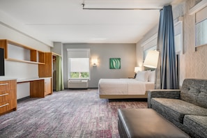 A hotel room with a bed, a sofa, a desk, and a wardrobe. - Home2 Suites by Hilton Albany Wolf Rd (Albany)