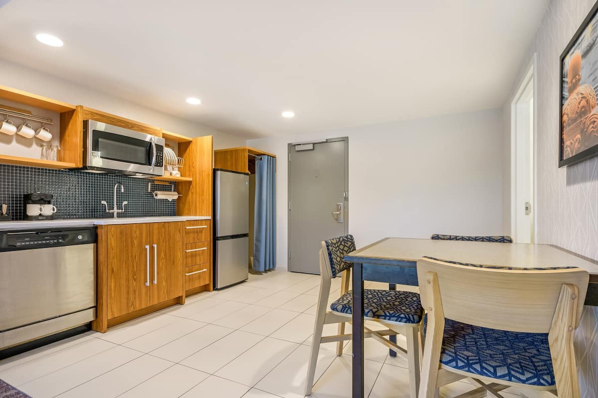 A modern kitchen with wooden cabinets, stainless steel appliances, a dining table with chairs, and a tiled floor.
