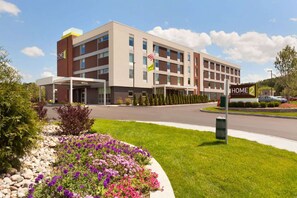 A modern hotel with a two-story structure, a covered entrance, and a landscaped garden with purple flowers. - Home2 Suites by Hilton Albany Wolf Rd (Albany)