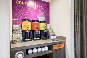A coffee and tea station with labeled dispensers for gourmet, hot water, and decaf options, along with mugs and trash receptacles. - Home2 Suites by Hilton Albany Wolf Rd (Albany)