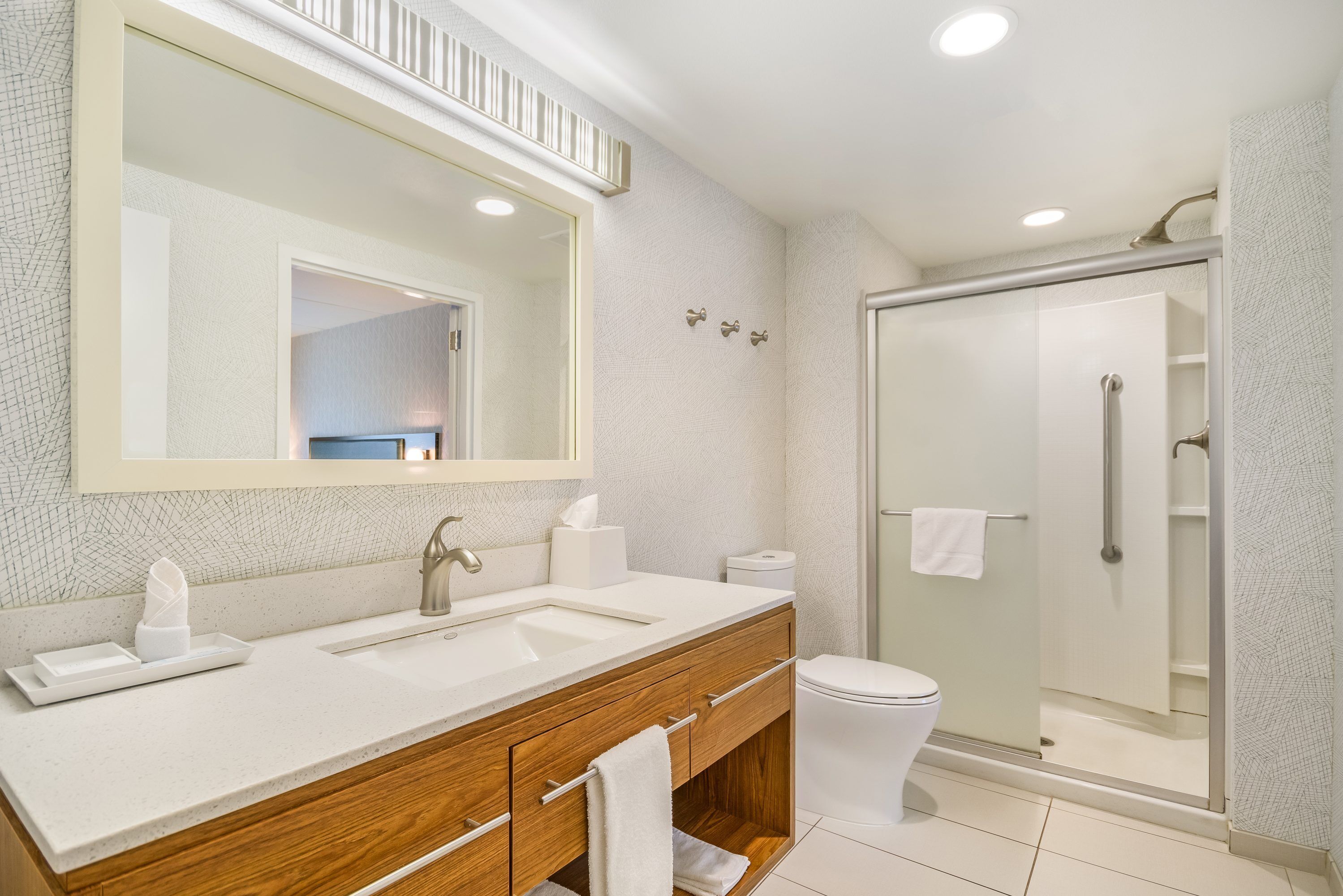 A modern bathroom with a large mirror, dual sinks, a toilet, and a glass-enclosed shower.