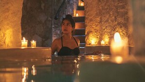 A person in a spa bath with candles and a stone wall.