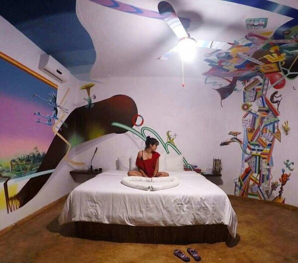 Un dormitorio con cama, ventilador de techo y una pared con arte abstracto.