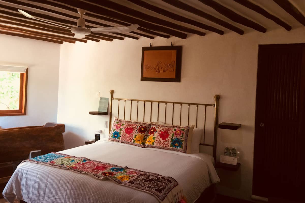 Une chambre à coucher avec un lit, un ventilateur de plafond, une tête de lit en bois, une table de chevet, une commode, un tableau encadré et une fenêtre.