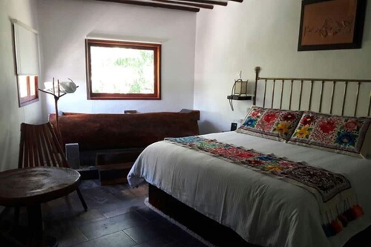 Une chambre à coucher comprenant un lit, un banc, une chaise, une fenêtre et un luminaire fixé au mur.