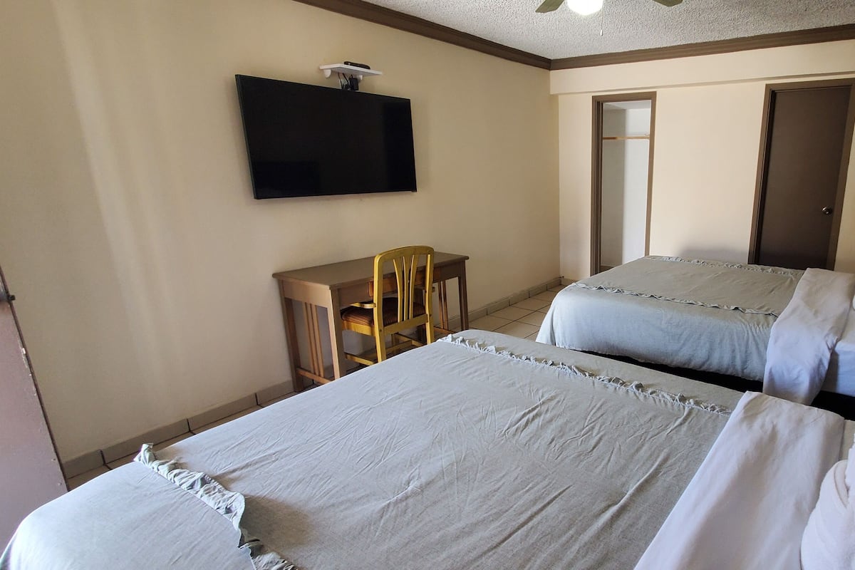 A hotel room with two beds, a desk, a chair, a television, and a door.