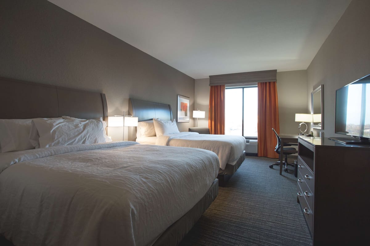 A hotel room with two beds, a desk, a chair, a television, and a window with curtains.