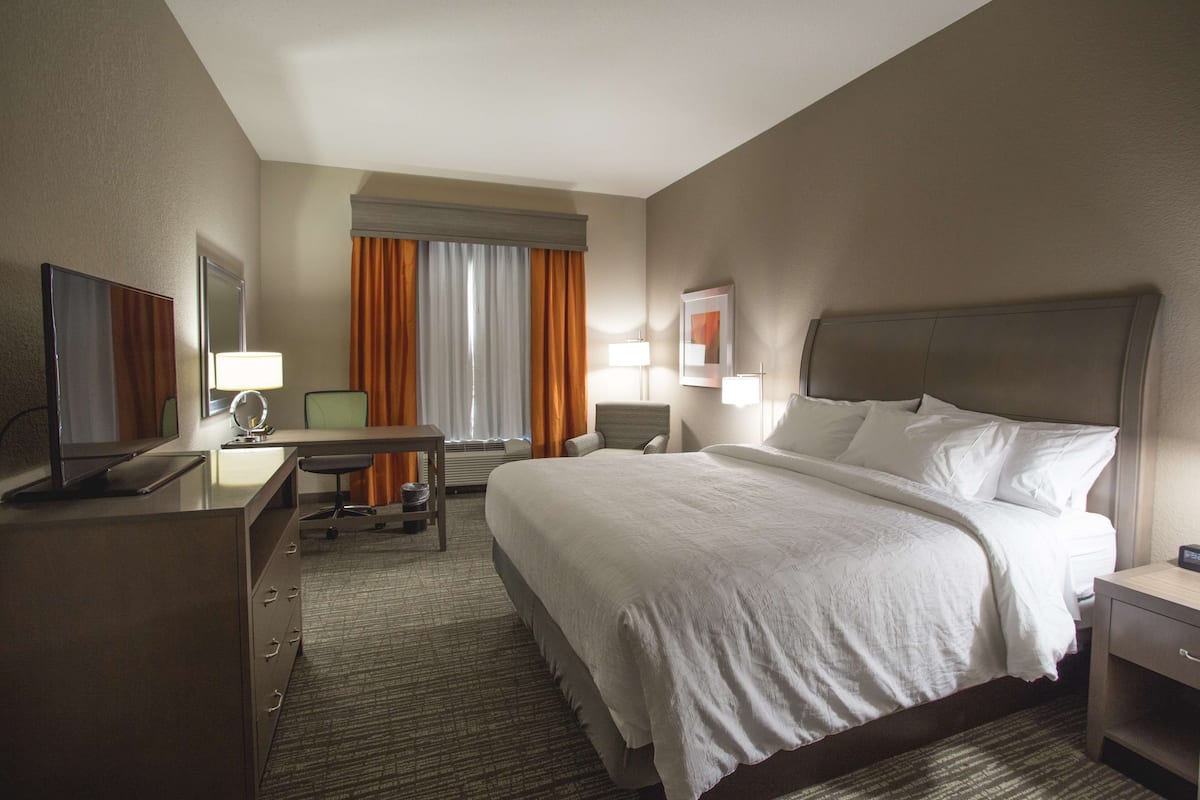 A hotel room with a large bed, a desk with a computer, a TV, and a chair.