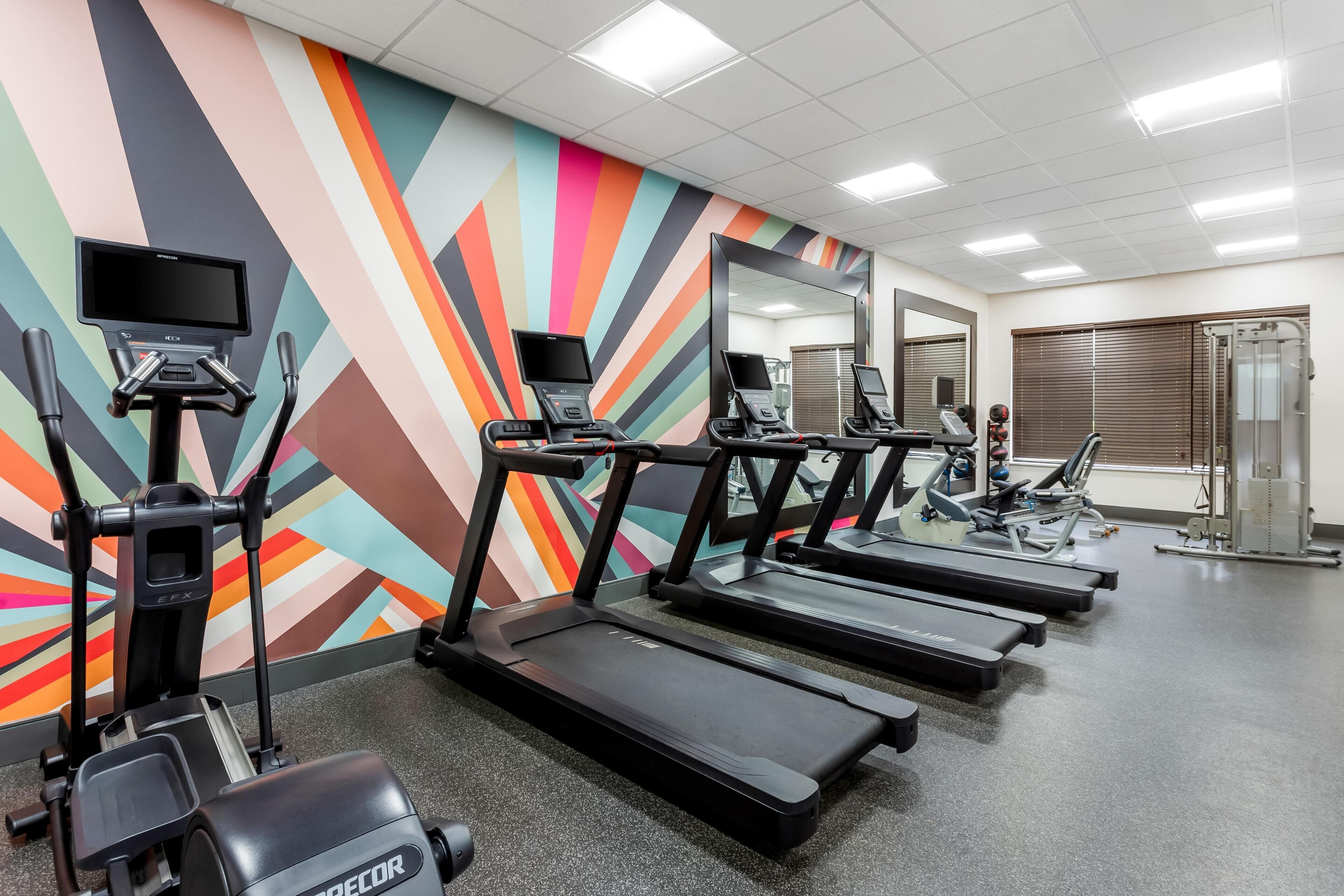 A gym with treadmills, exercise bikes, and a colorful wall.