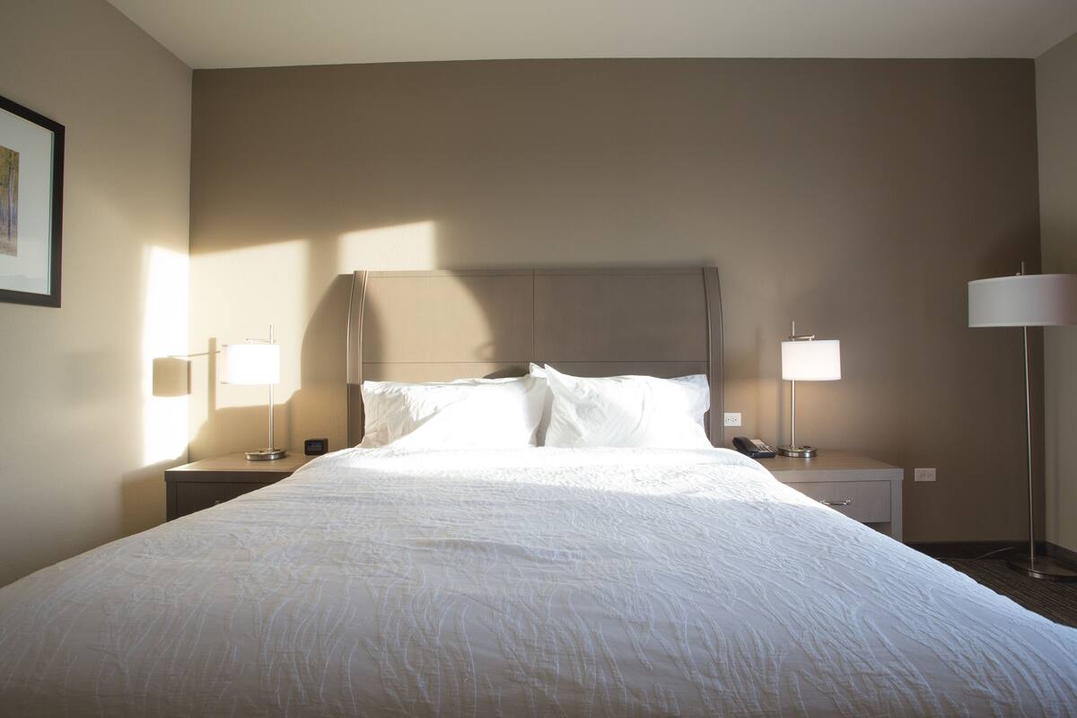 A neatly made bed with white linens, two bedside lamps, and a nightstand with a lamp.