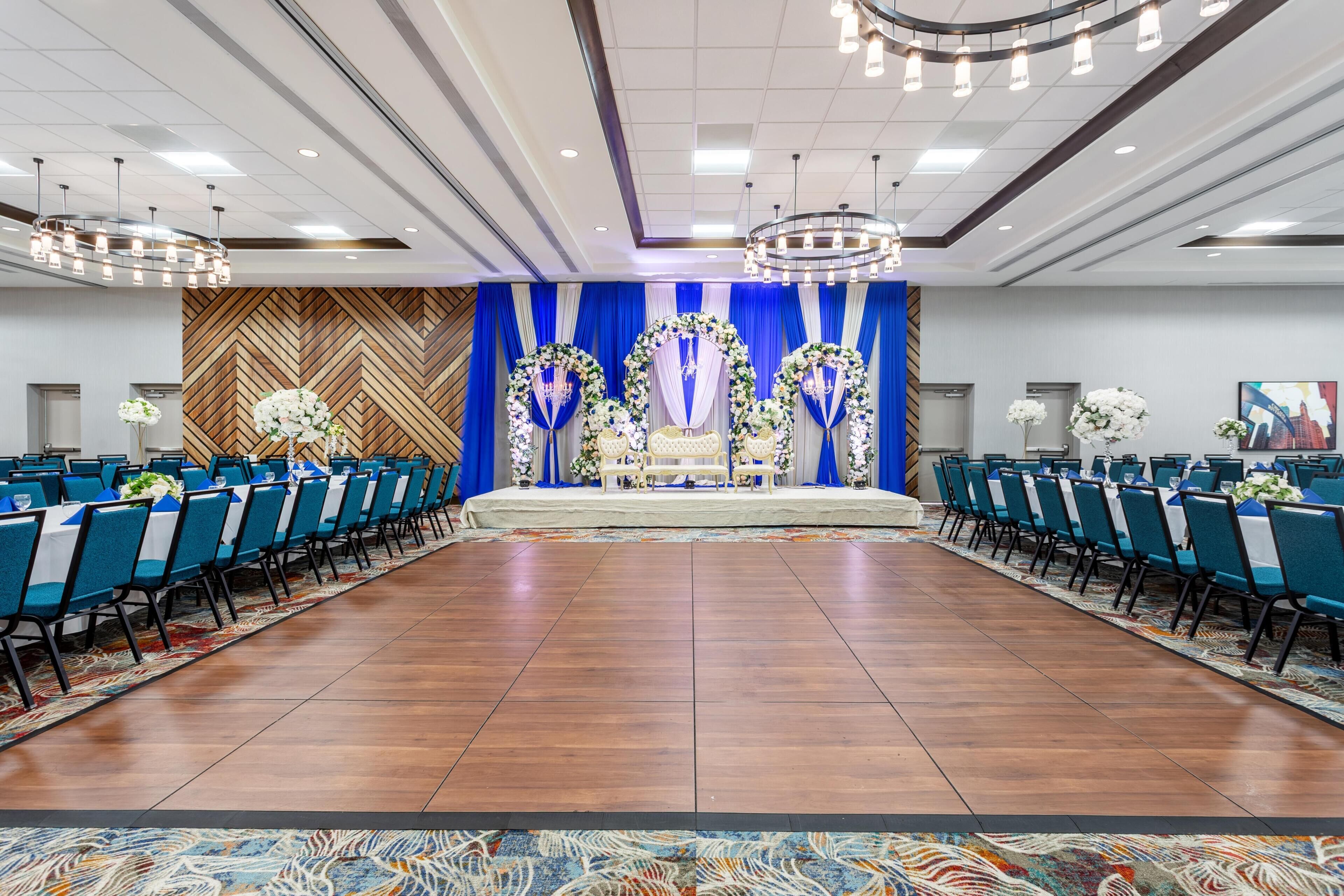 Une salle de conférence dotée d’une scène, de chaises bleues et d’un tapis à motifs.