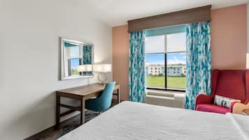 A hotel room with a bed, a desk, a chair, a window with curtains, and a view of buildings outside.