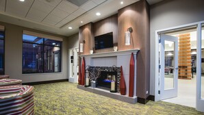 A hotel lobby with a fireplace, striped seating, and a large window. - Hilton Garden Inn Bolingbrook I-55 (Bolingbrook)