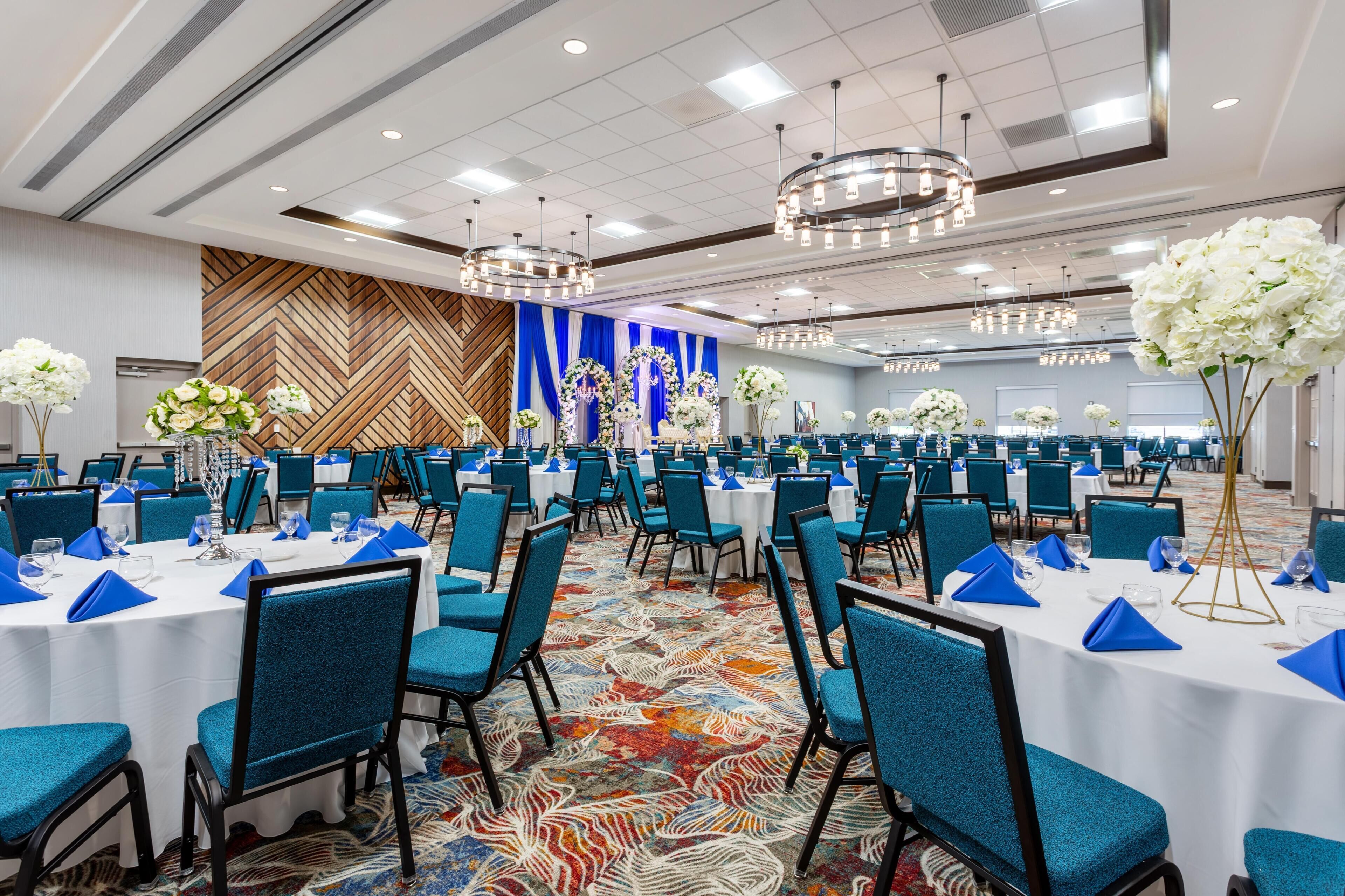 A banquet hall with round tables, blue chairs, and floral centerpieces.